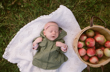 a baby lays sleeping next to a basket of apples