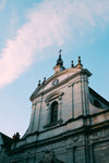 a baroque church points a crucifix at the blue sky