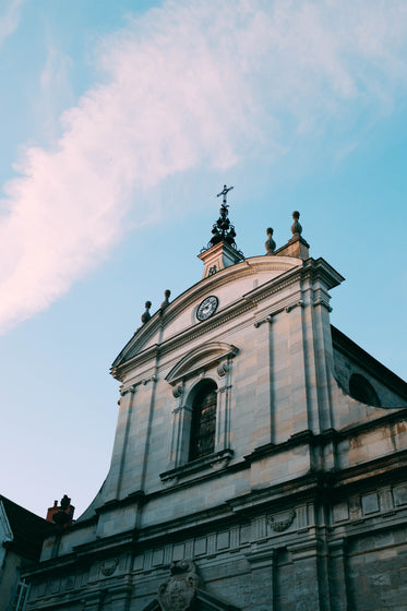 a baroque church points a crucifix at the blue sky