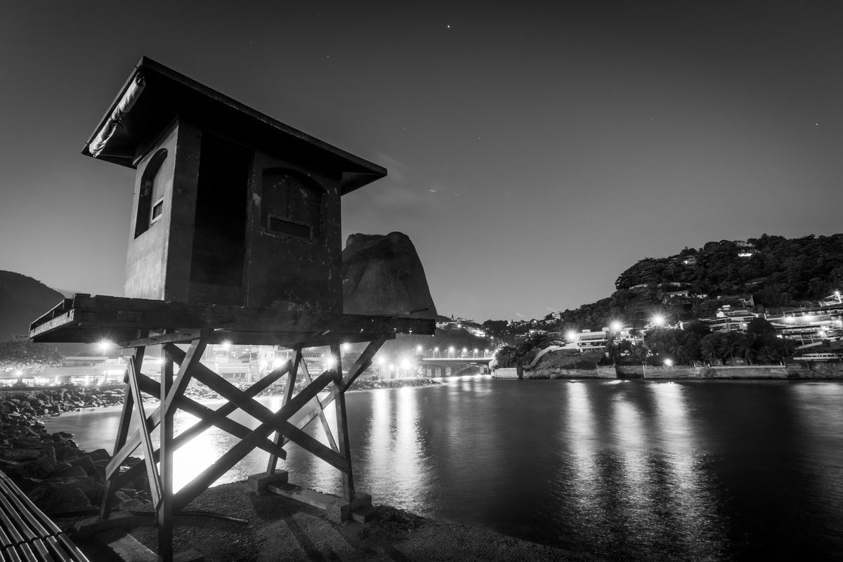 a battered hut at the water's edge framed by city lights