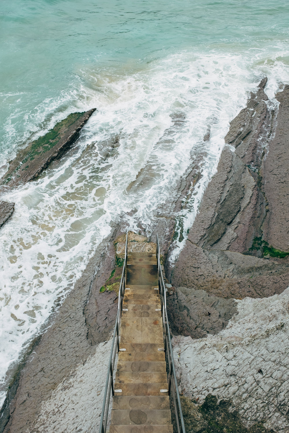 a bird's eye view of wooden steps to the foaming sea below