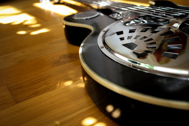 a black guitar reflects sunlight onto the wooden floor
