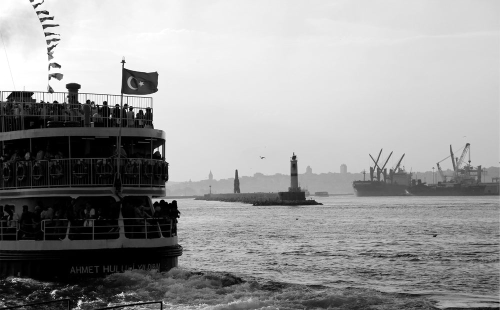 a boat full of people sailing away in black and white