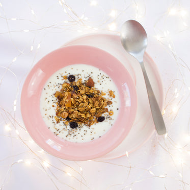 a bowl of muesli in a pink bowl on a saucer with spoon