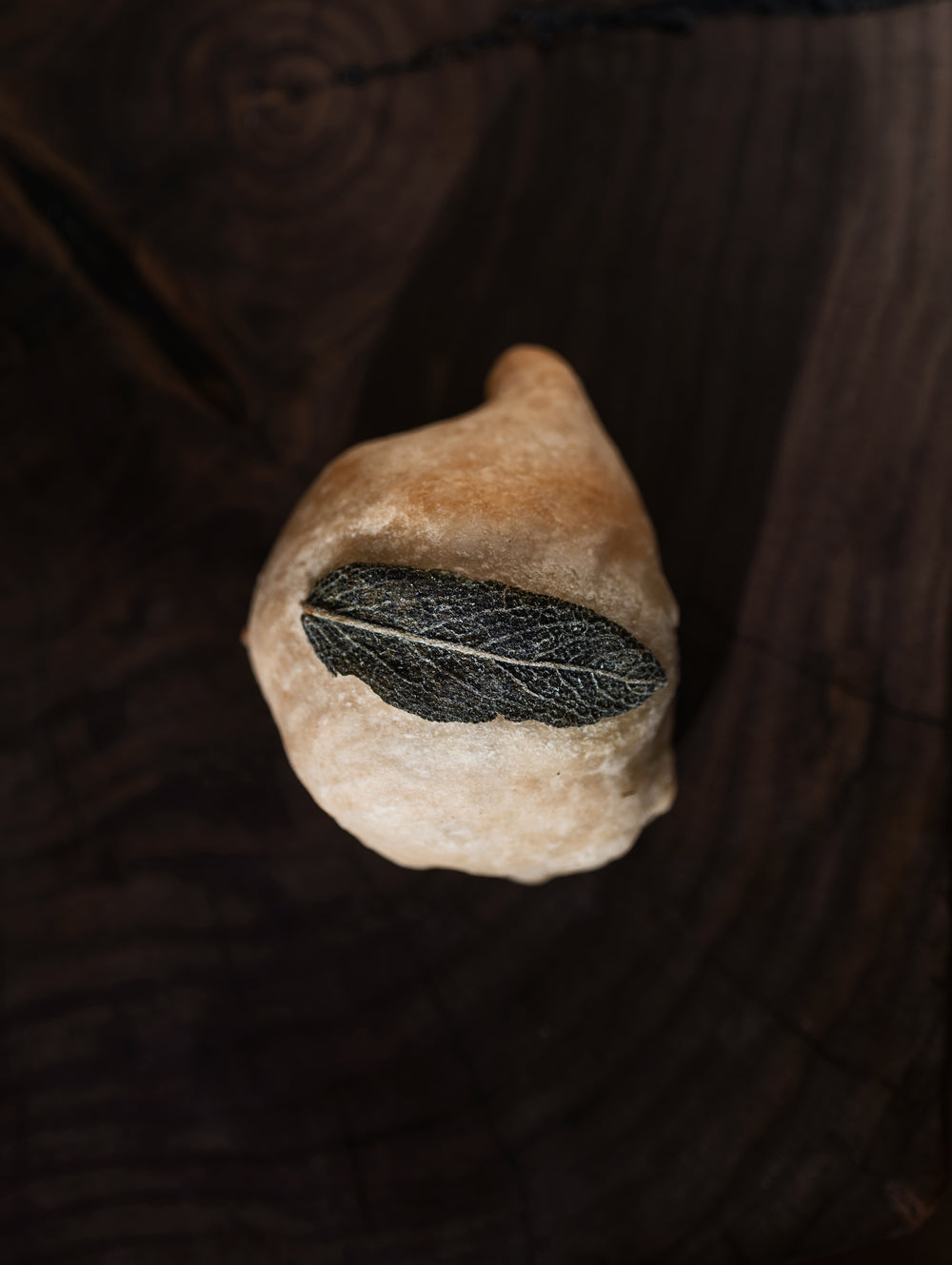 a bun topped with a sage leaf on a cutting board