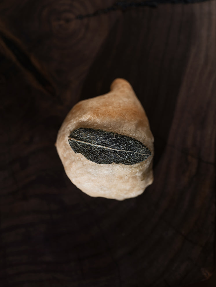 A Bun Topped With A Sage Leaf On A Cutting Board