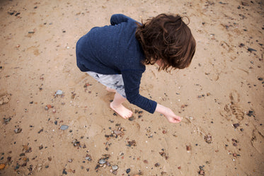 a child with long brown hair inspects pebbles on the beach