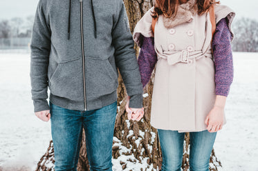 a couple braving the winter in front of a tall tree