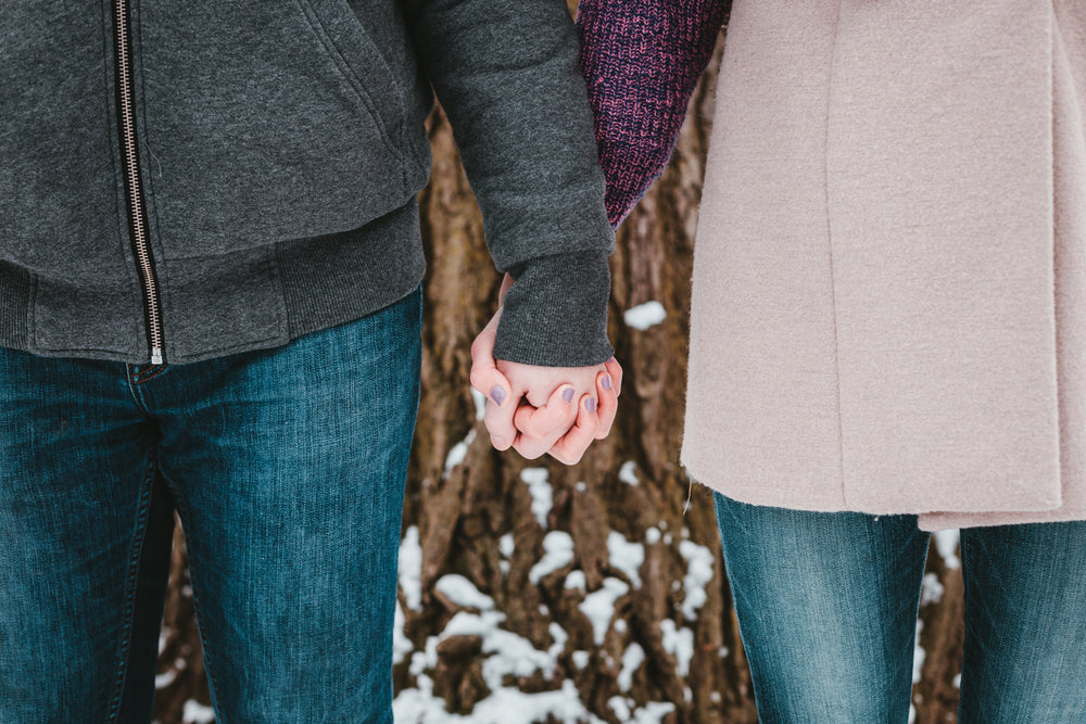 a couple holds hands by a snow-covered tree
