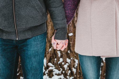 a couple holds hands by a snow-covered tree