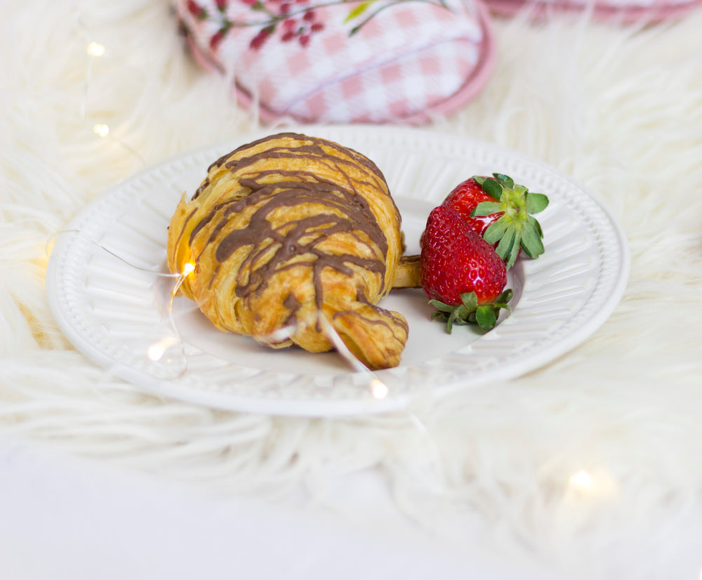 a croissant laced with chocolate on a white paper plate