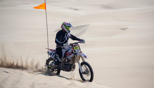 a dirt bike racer spins sand riding over dunes