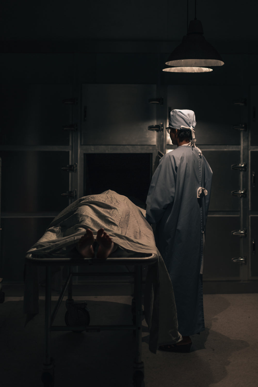 a doctor in scrubs puts a corpse into a mortuary freezer