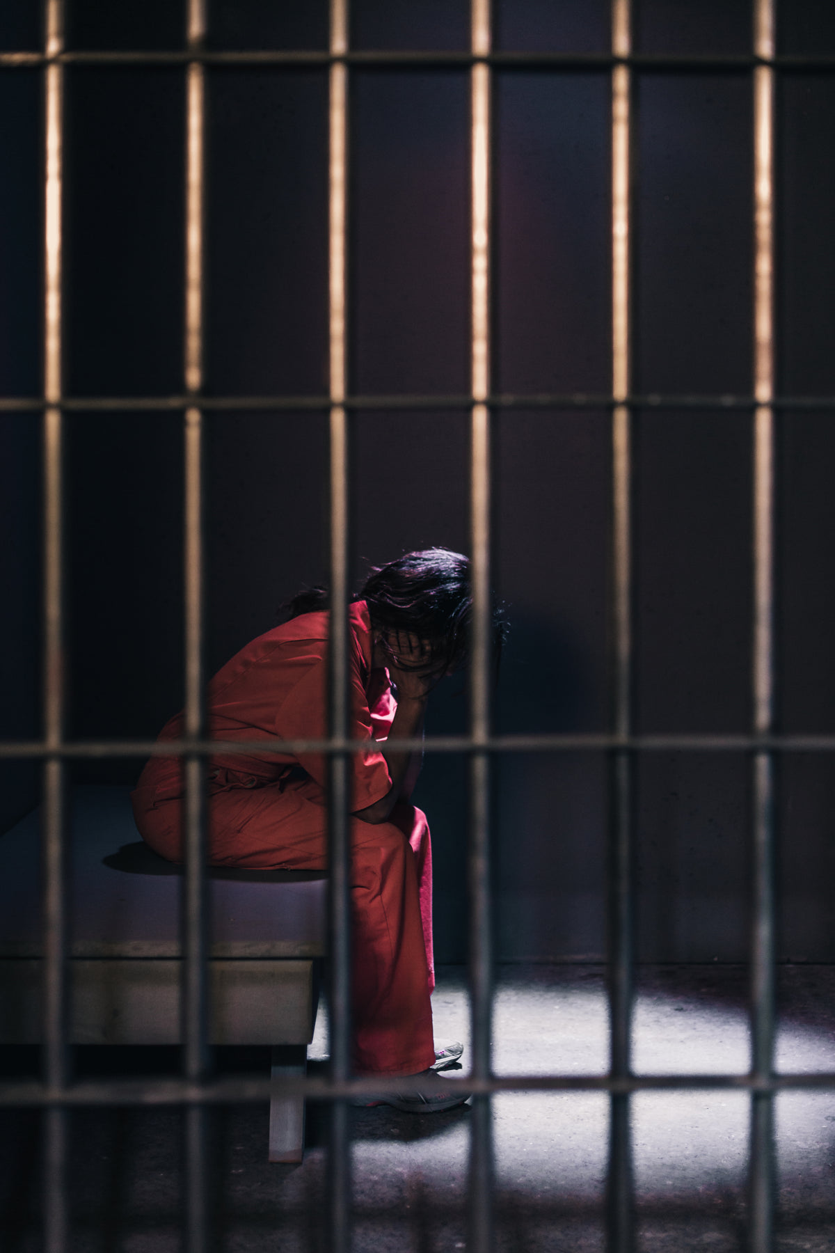 一名女囚双手抱头坐在牢房的床上