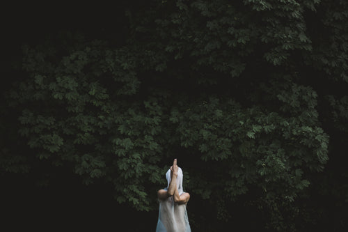 a figure in white gauze strikes a pose in the woods