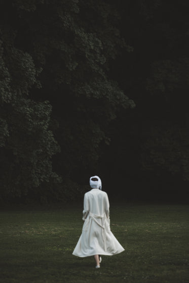 a figure in white gauze walks towards the woods