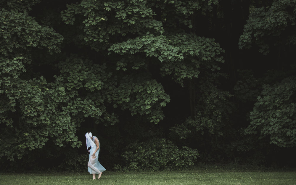 a figure in white tip toes on the edge of the woods