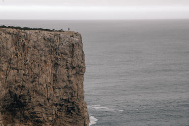 a figure on a cliff overlooking the ocean under a grey sky