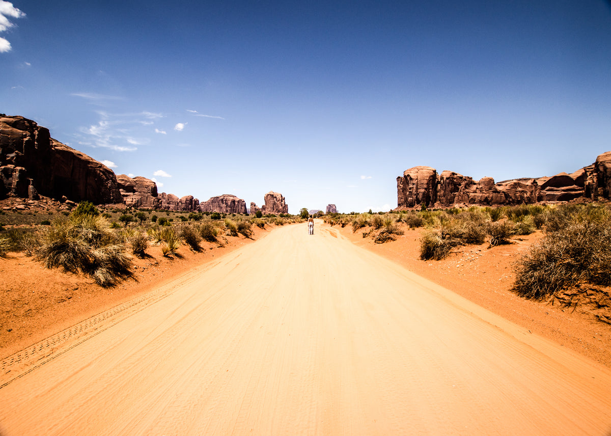 a figure stands on a road in the desert under blue skies