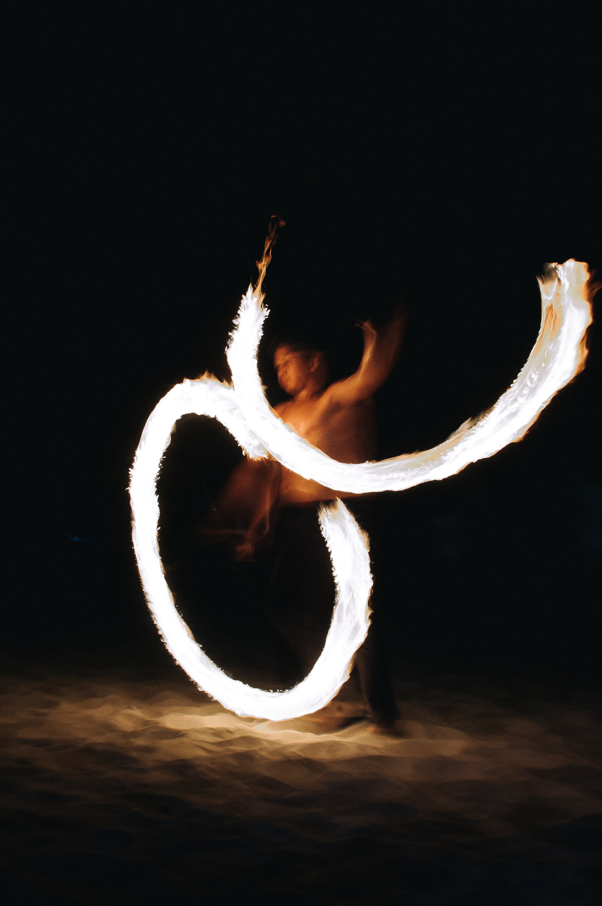 a fire dancer cuts figures of eight at night on a beach