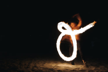 a fire dancer draws shapes on a beach at night