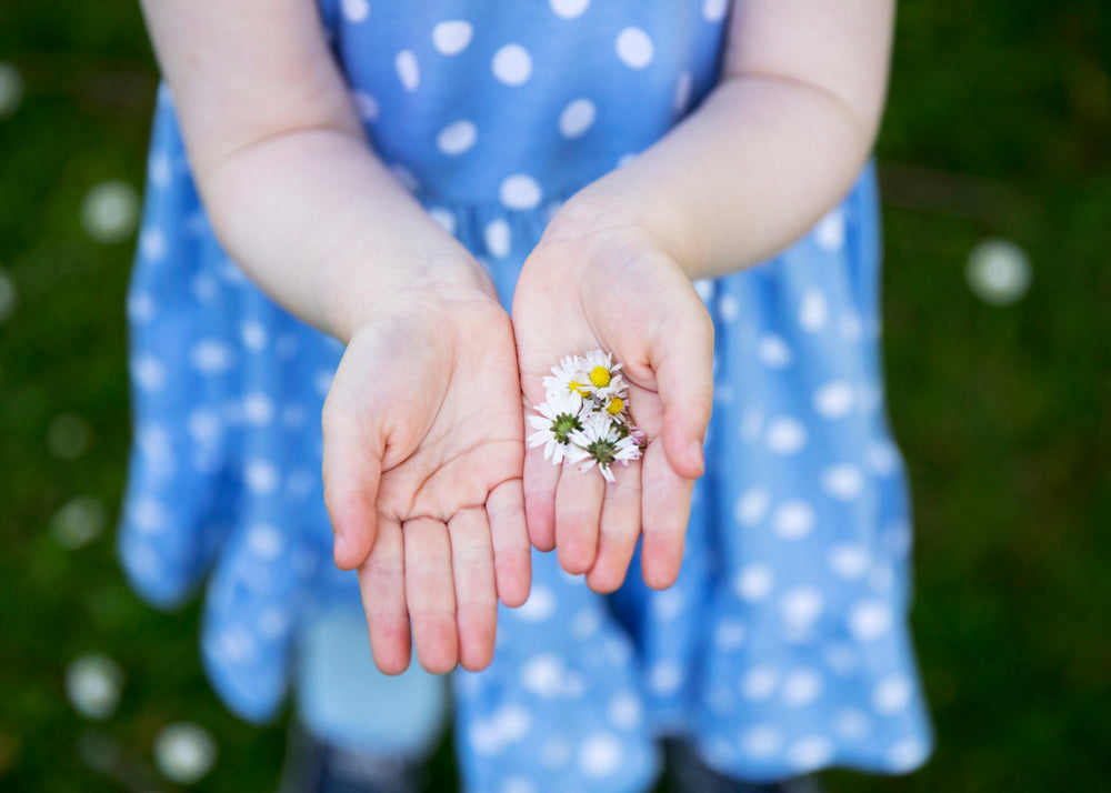 a girl in a polkadot dress holds out dandelions