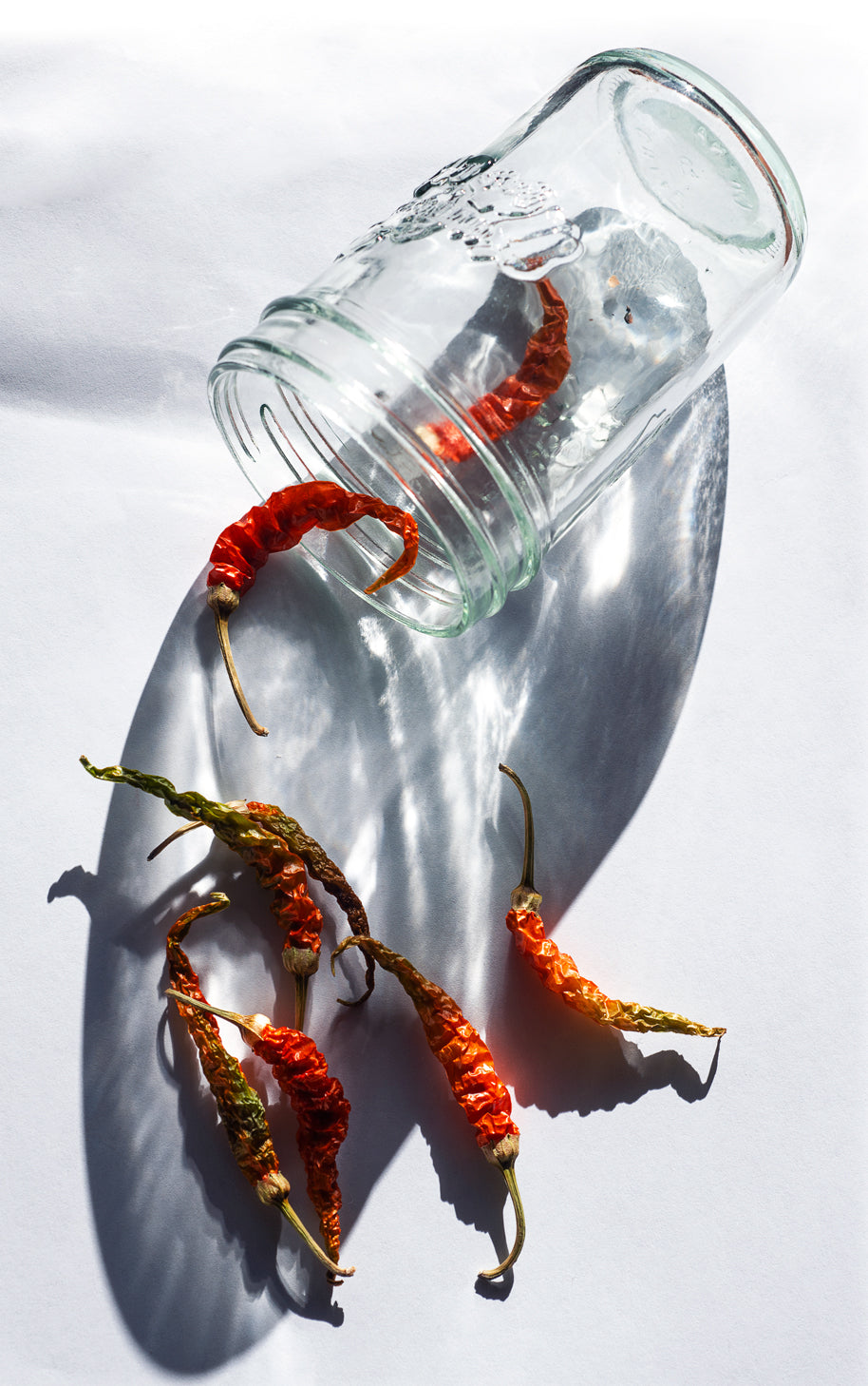 a glass jar with red chili peppers falling out of it