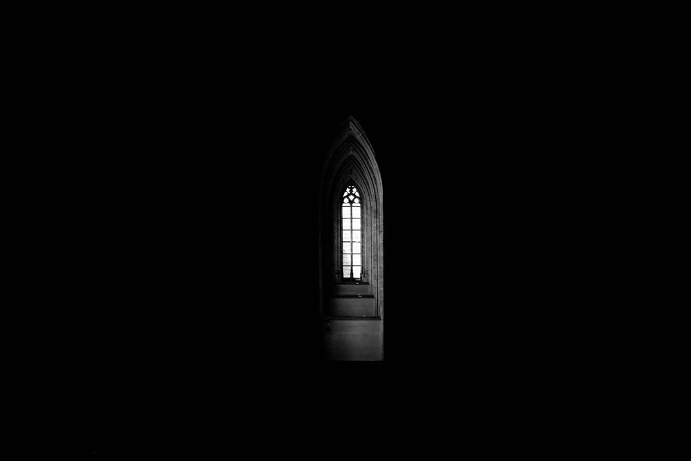 a gothic church window spills light into interior darkness