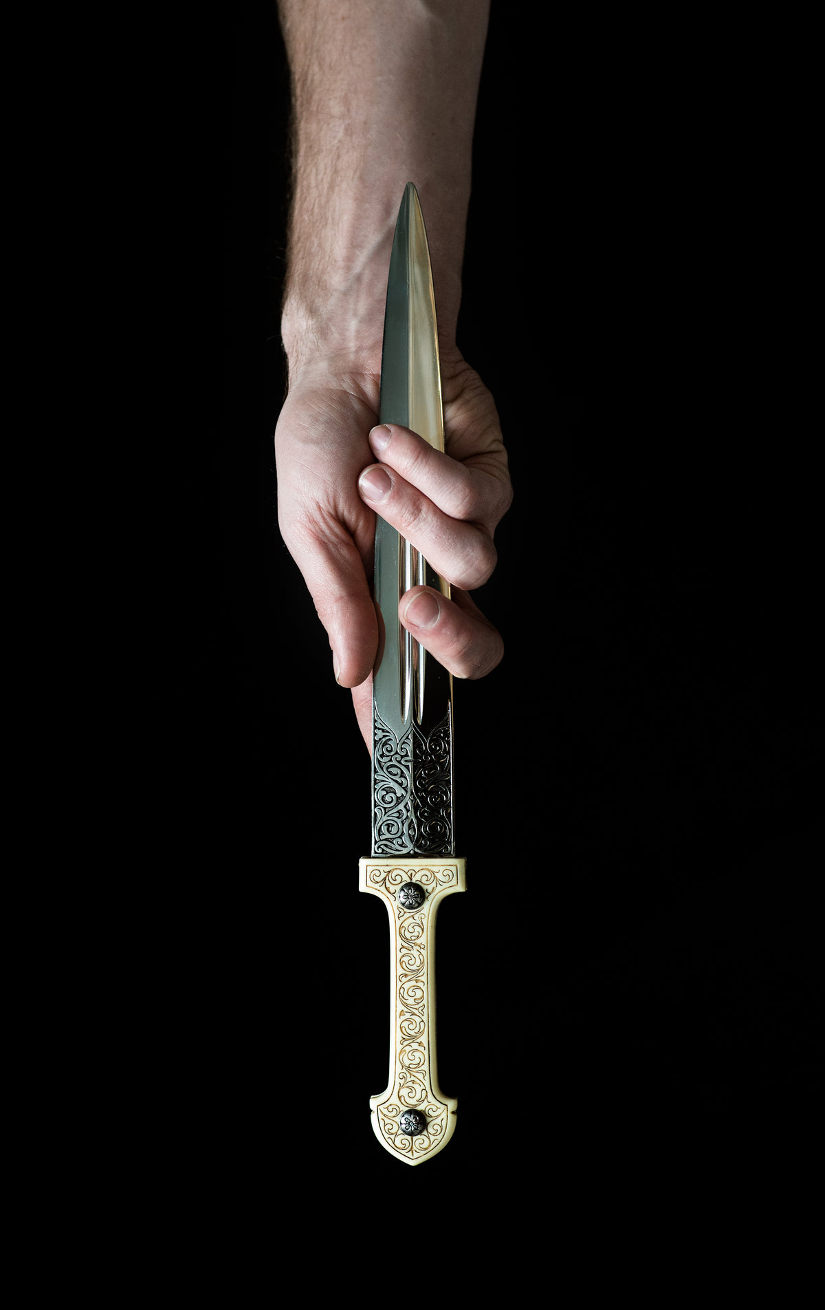 a hand clasps an ornate dagger by the blade