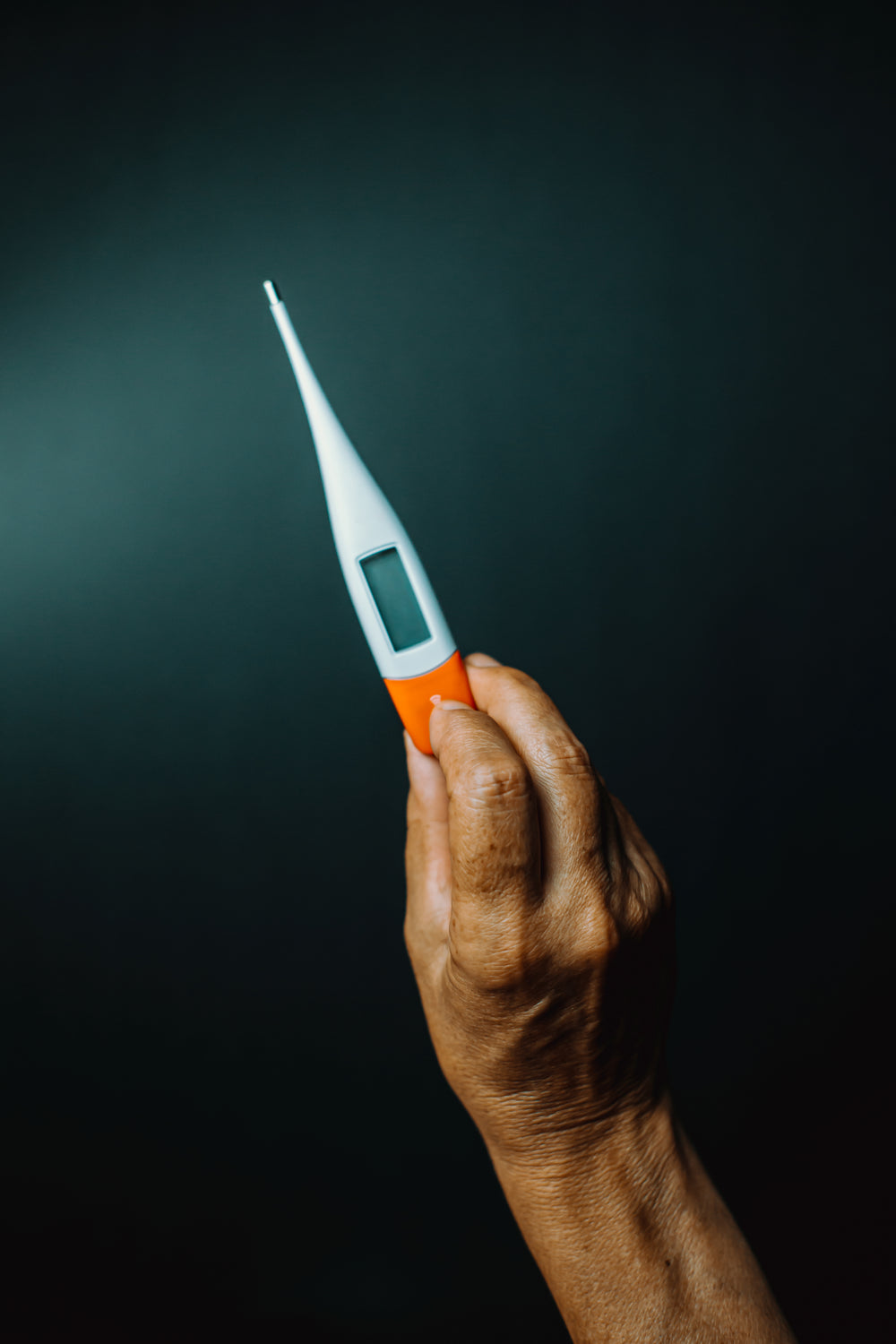 a hand holds up a thermometer against black background