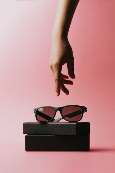 a hand reaches for black sunglasses sitting on a case