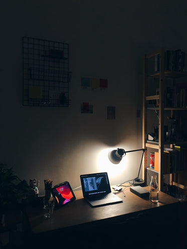 a laptop and tablet beam from a desktop backlit by a lamp