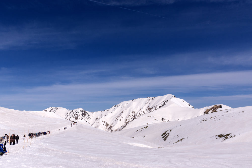 a line of hikers travel across the snow capped mountains