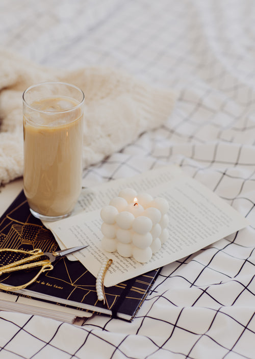 a lit candle with iced coffee and hair accessories