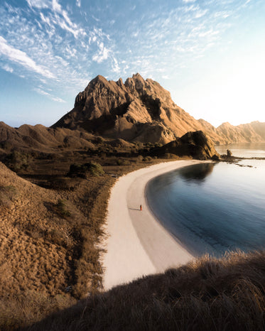 a lone figure on a beach against a mountain in distance