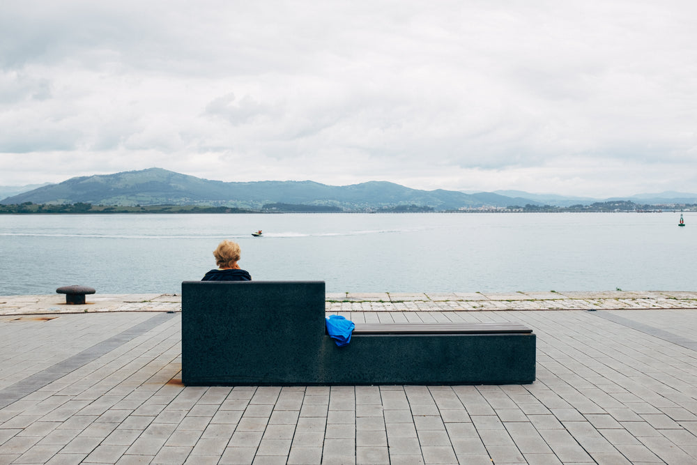 a lone woman sits on a bench watching jet skiers on water