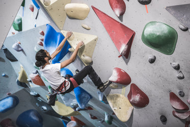 a man hangs from the side of a rock climbing wall