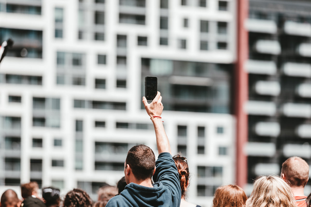 a man holds up a mobile in a crowd on a bright day