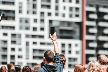 a man holds up a mobile in a crowd on a bright day