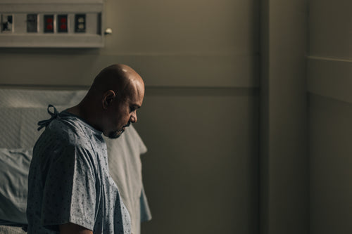 a man in a hospital room stares down at the floor