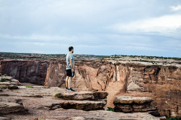 a man on a rocky plateau overlooks a deep canyon