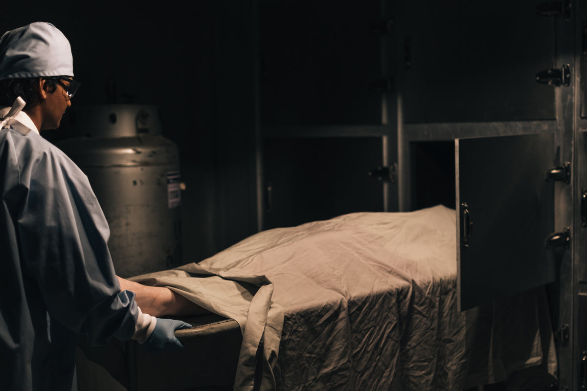 a man pushes a body on a tray into the freezer in the morgue
