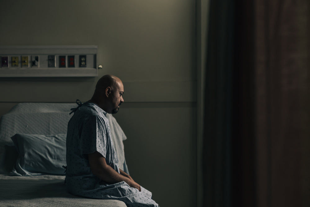 a man sits on his hospital bed and stares at the ground