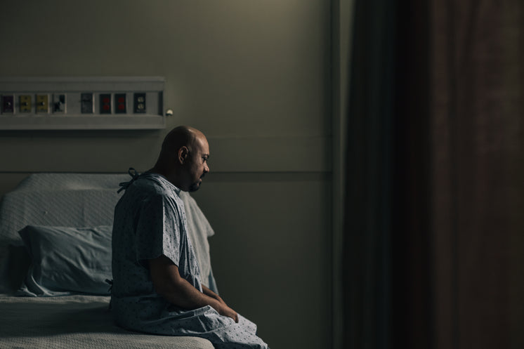 A Man Sits On His Hospital Bed And Stares At The Ground