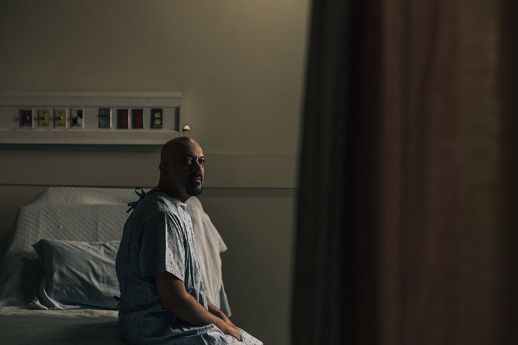 A Man Sits On His Hospital Bed And Stares Into The Distance