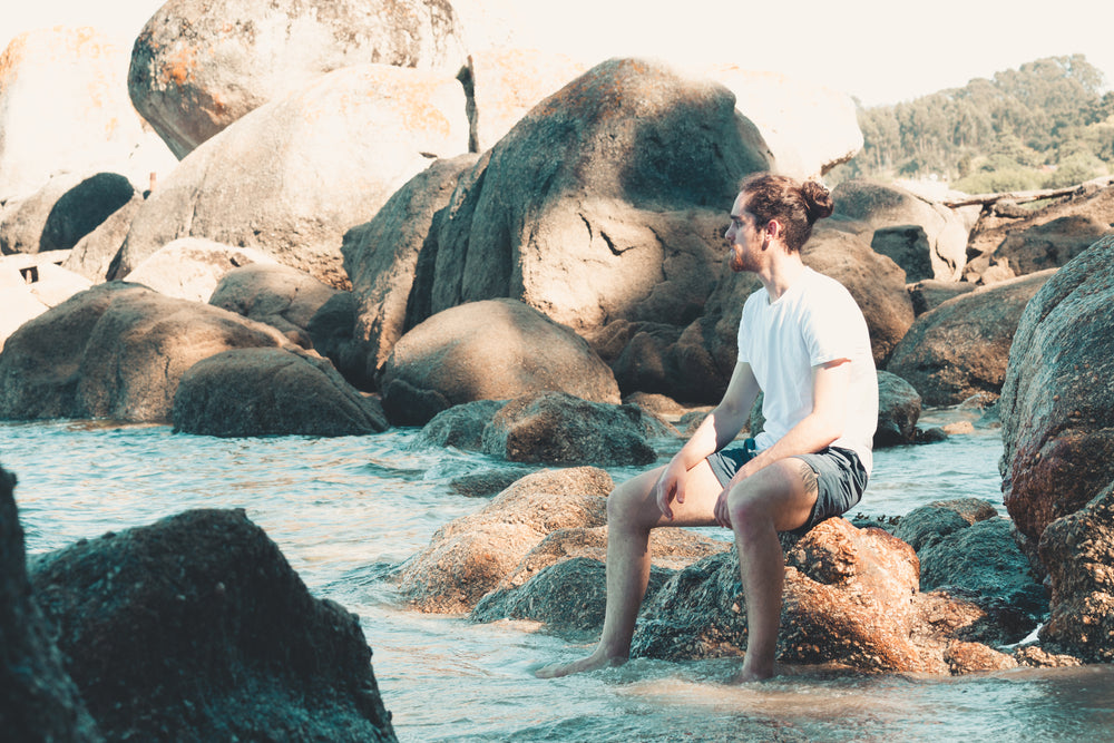 a man sitting on a rock with his feet dipped in the water