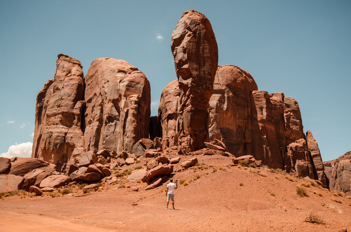 a man with a camera stands small against red desert pillars