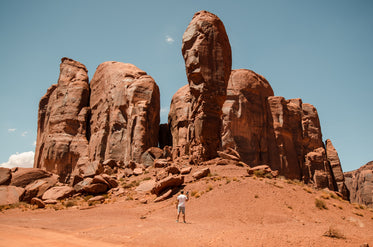 a man with a camera stands small against red desert pillars