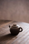 a mini brown teapot with carved characters on a wooden tabletop