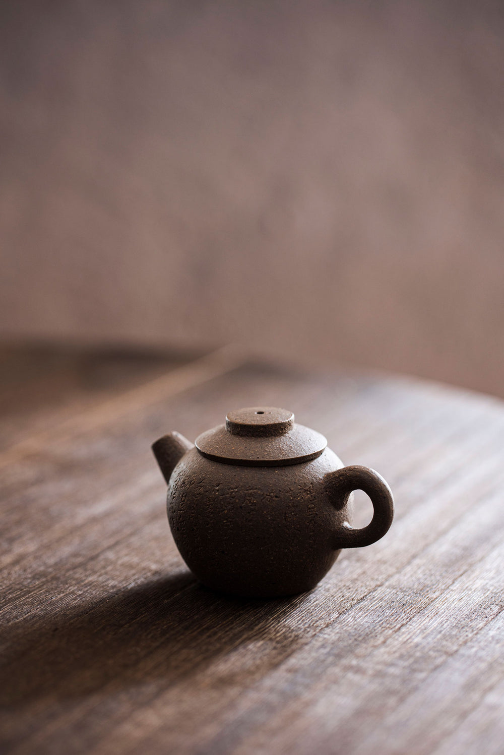 a mini brown teapot with carved characters on a wooden tabletop